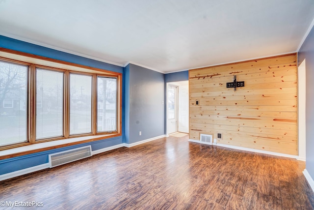 empty room featuring dark hardwood / wood-style flooring, ornamental molding, and wooden walls