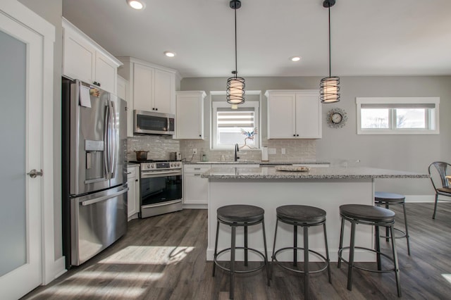 kitchen featuring a kitchen island, white cabinetry, appliances with stainless steel finishes, and hanging light fixtures