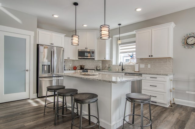 kitchen with stainless steel appliances, white cabinetry, hanging light fixtures, and a kitchen island