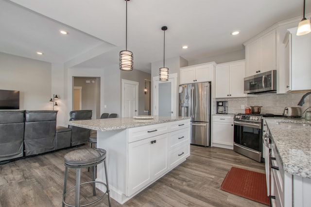 kitchen featuring a kitchen island, appliances with stainless steel finishes, white cabinets, and decorative light fixtures