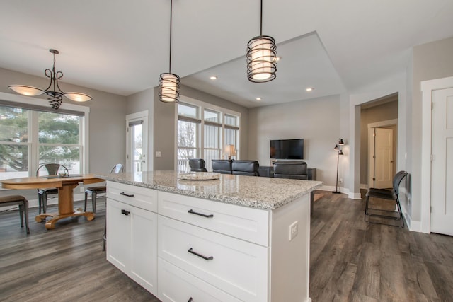 kitchen featuring dark wood-type flooring, white cabinetry, decorative light fixtures, a center island, and light stone countertops