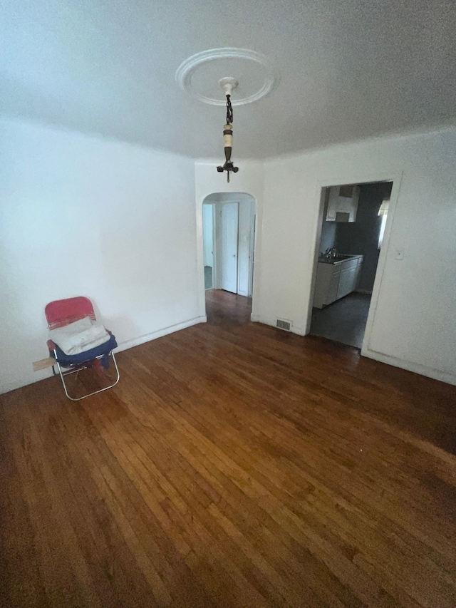 unfurnished dining area featuring visible vents, a textured ceiling, arched walkways, and wood finished floors