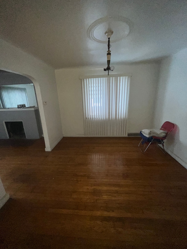 unfurnished dining area featuring arched walkways, a fireplace with raised hearth, and wood finished floors