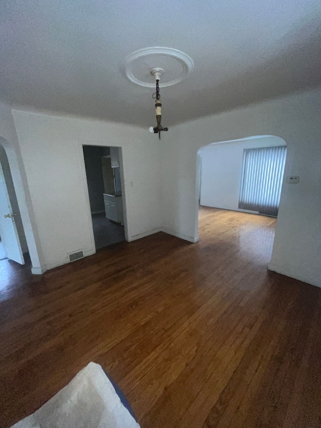 unfurnished dining area featuring arched walkways, wood finished floors, and visible vents