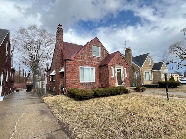 tudor-style house featuring a front yard, brick siding, an outdoor structure, and a chimney