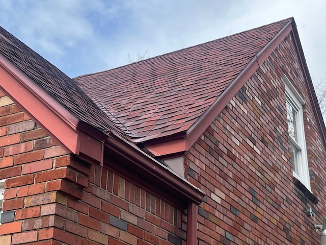 exterior details featuring a shingled roof and brick siding