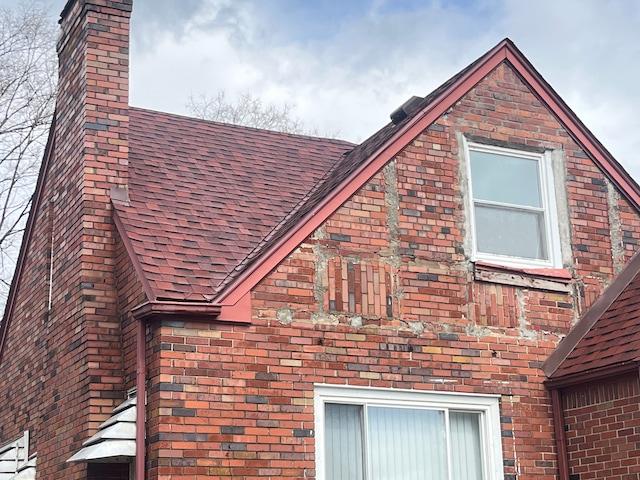 view of side of home with a shingled roof, brick siding, and a chimney