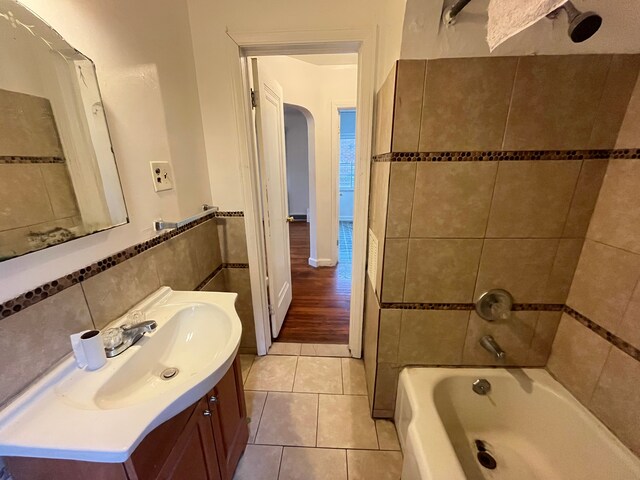 bathroom featuring vanity, tile patterned flooring,  shower combination, a wainscoted wall, and tile walls