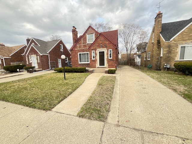 tudor home featuring concrete driveway, a front yard, and brick siding