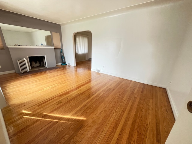 unfurnished living room with visible vents, baseboards, arched walkways, a fireplace with raised hearth, and wood finished floors