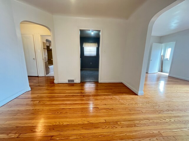 unfurnished room featuring arched walkways, light wood finished floors, baseboards, and visible vents