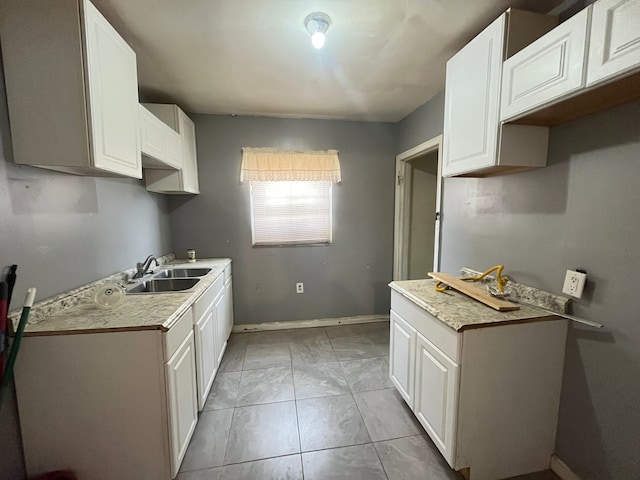 kitchen with a sink, light countertops, white cabinetry, and baseboards