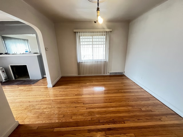 empty room featuring a fireplace, arched walkways, visible vents, wood finished floors, and baseboards