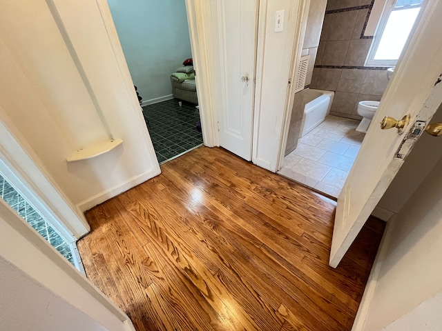 bathroom with a bathing tub, toilet, and wood finished floors