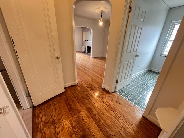 hall featuring baseboards, arched walkways, and wood finished floors