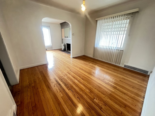 empty room featuring baseboards, a fireplace, visible vents, arched walkways, and wood finished floors