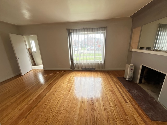 unfurnished living room featuring a fireplace with flush hearth, light wood finished floors, and baseboards