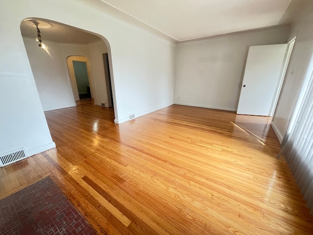 unfurnished room featuring visible vents, baseboards, light wood finished floors, and arched walkways