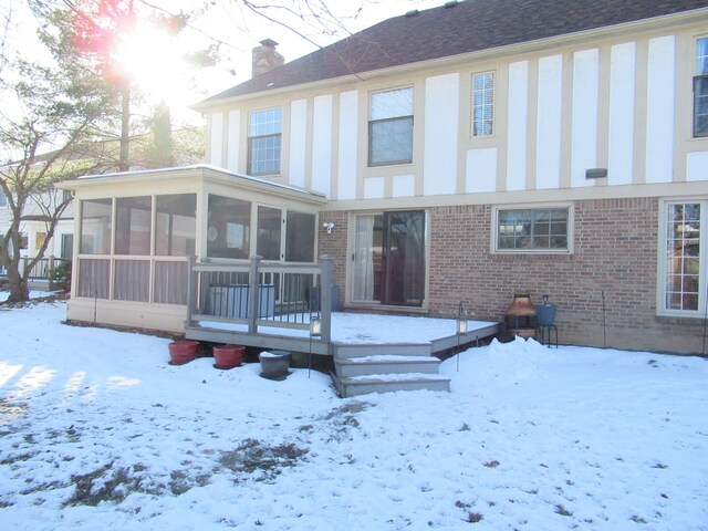 snow covered property with a wooden deck and a sunroom