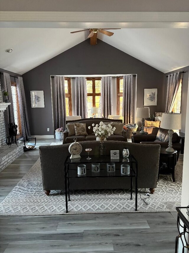 living room with a brick fireplace, dark wood-type flooring, vaulted ceiling with beams, and ceiling fan