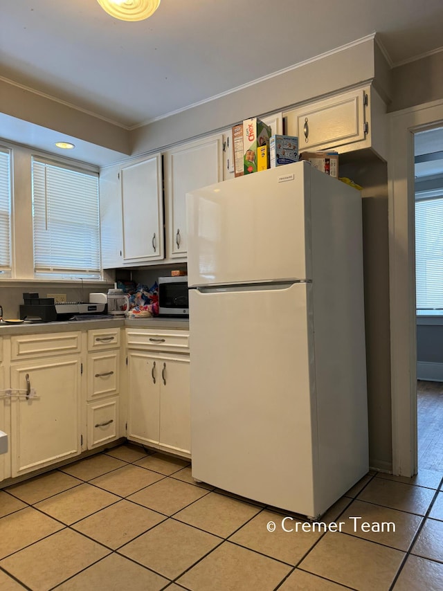 kitchen featuring light tile patterned floors, ornamental molding, white cabinets, and white fridge