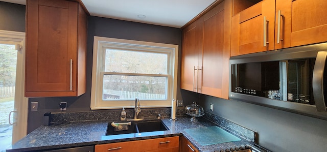 kitchen with appliances with stainless steel finishes, a wealth of natural light, sink, and dark stone countertops