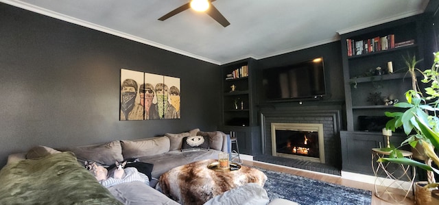 living room featuring crown molding, a brick fireplace, built in shelves, and ceiling fan