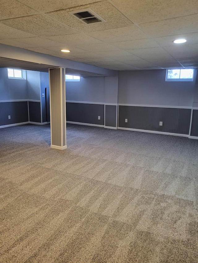 basement featuring a paneled ceiling, wood walls, and carpet flooring