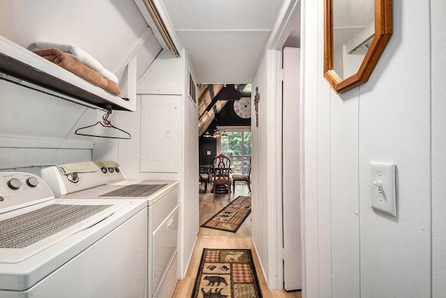 clothes washing area with washing machine and dryer, light wood-type flooring, and wood walls