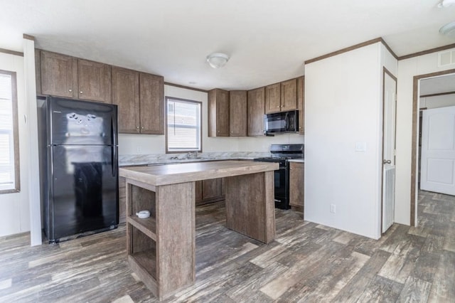 kitchen featuring dark wood-type flooring, ornamental molding, a center island, and black appliances