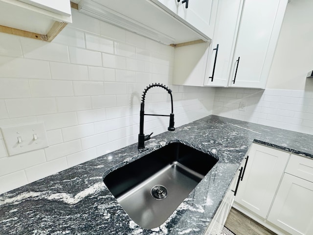 kitchen featuring sink, white cabinetry, hardwood / wood-style flooring, dark stone counters, and backsplash