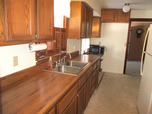 kitchen featuring white refrigerator, sink, light colored carpet, and wooden counters