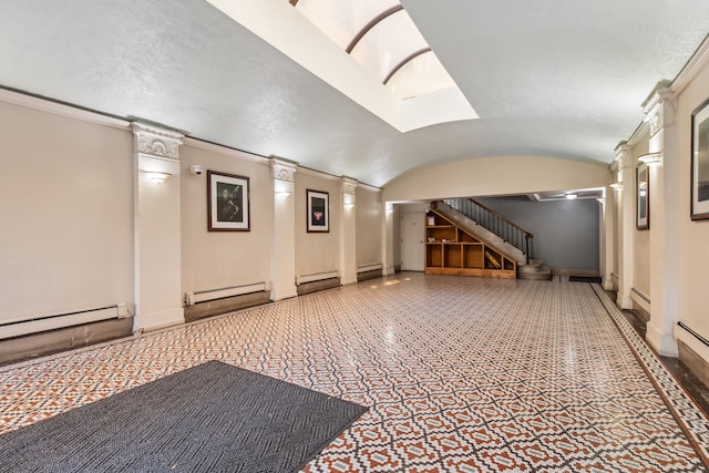 interior space featuring a baseboard heating unit, vaulted ceiling, and ornate columns