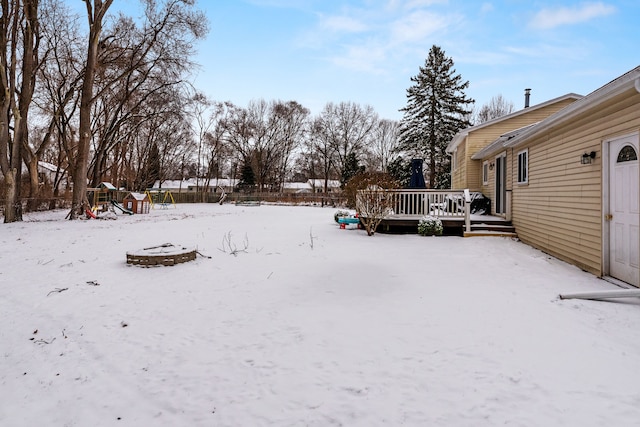 snowy yard with a playground and a deck