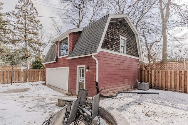 snow covered house featuring a garage and central air condition unit