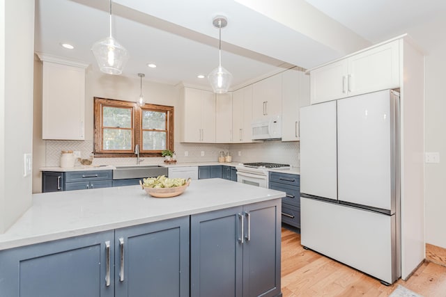 kitchen featuring pendant lighting, blue cabinets, white cabinetry, sink, and white appliances