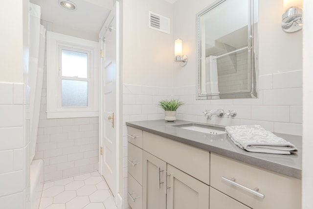 bathroom featuring tile patterned flooring, vanity, a shower, and tile walls