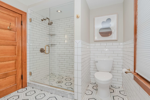 bathroom featuring tile patterned floors, toilet, a shower with shower door, and tile walls