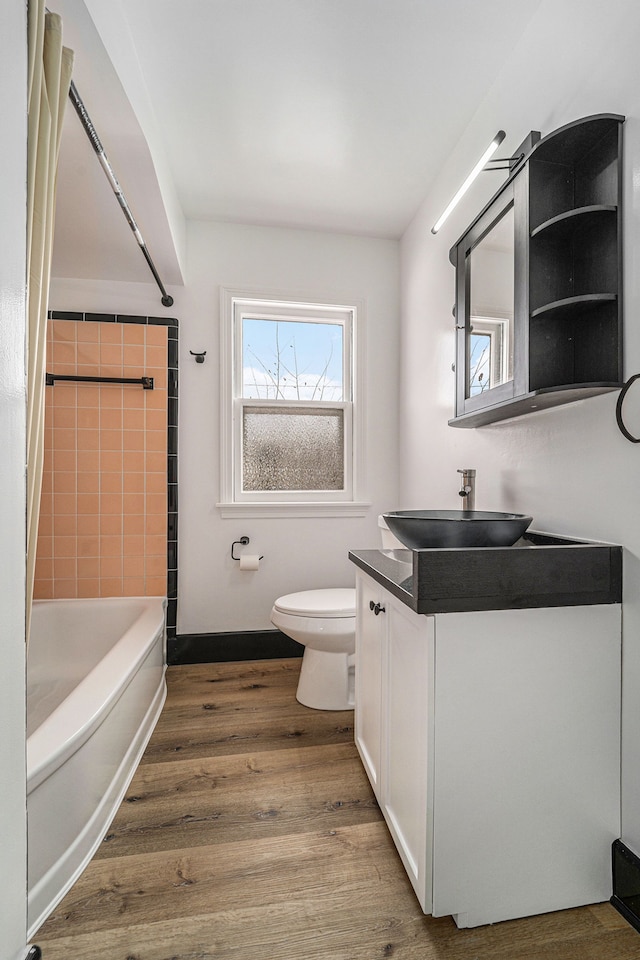 full bathroom with tiled shower / bath combo, vanity, hardwood / wood-style floors, and toilet