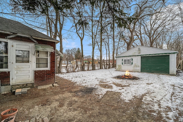 yard covered in snow with a garage, an outbuilding, and an outdoor fire pit