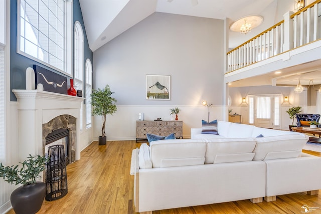 living room featuring a tiled fireplace, a notable chandelier, high vaulted ceiling, and light hardwood / wood-style flooring