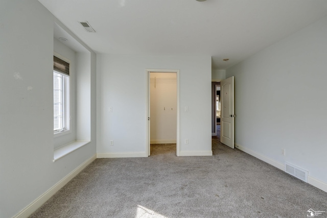 unfurnished bedroom with a walk in closet, light colored carpet, and a closet