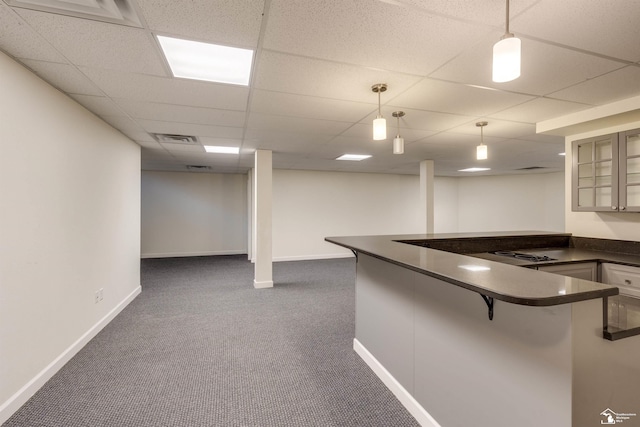 interior space with a paneled ceiling, pendant lighting, a kitchen bar, dark carpet, and kitchen peninsula