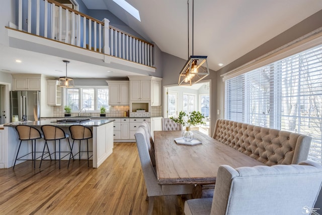 dining area with lofted ceiling with skylight, sink, and light hardwood / wood-style floors