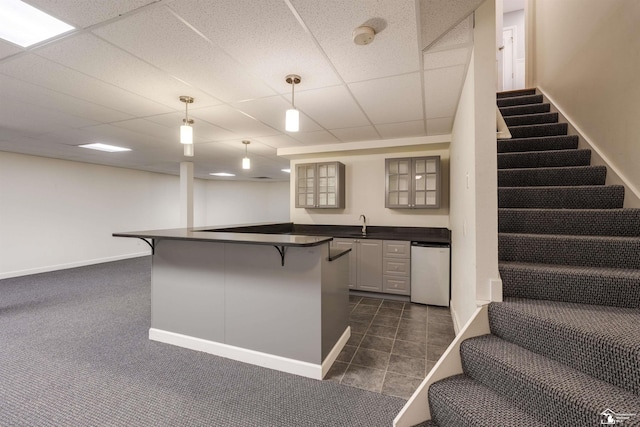 kitchen with decorative light fixtures, a kitchen bar, stainless steel dishwasher, kitchen peninsula, and a drop ceiling