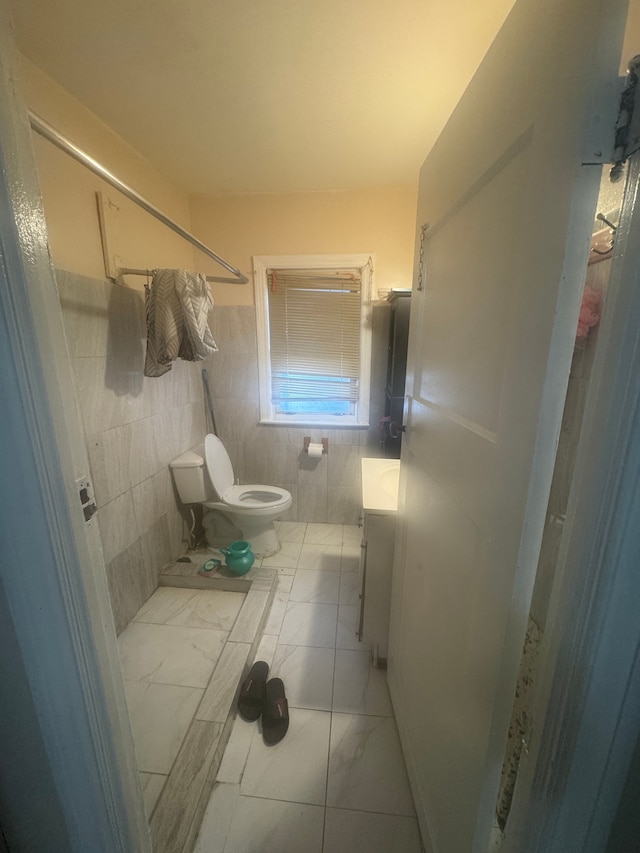 bathroom with vanity, a shower, tile walls, and toilet