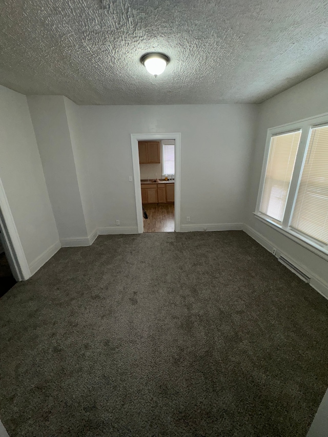 empty room with a textured ceiling and dark colored carpet