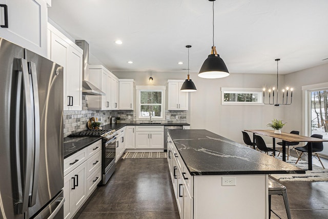 kitchen featuring wall chimney range hood, decorative light fixtures, stainless steel appliances, and white cabinets