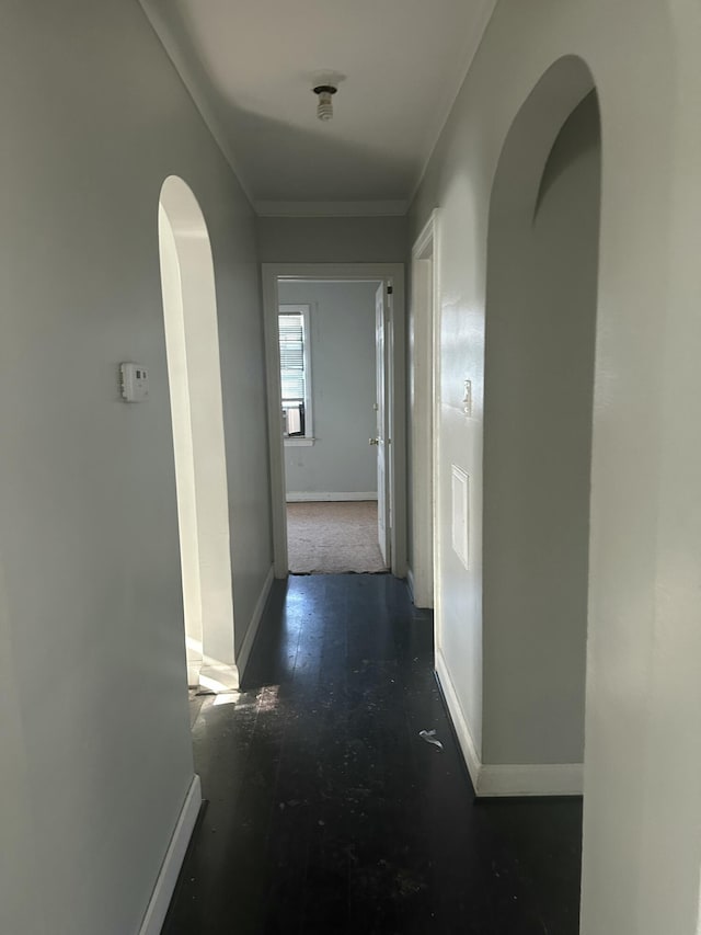 hall featuring arched walkways, crown molding, baseboards, and wood finished floors