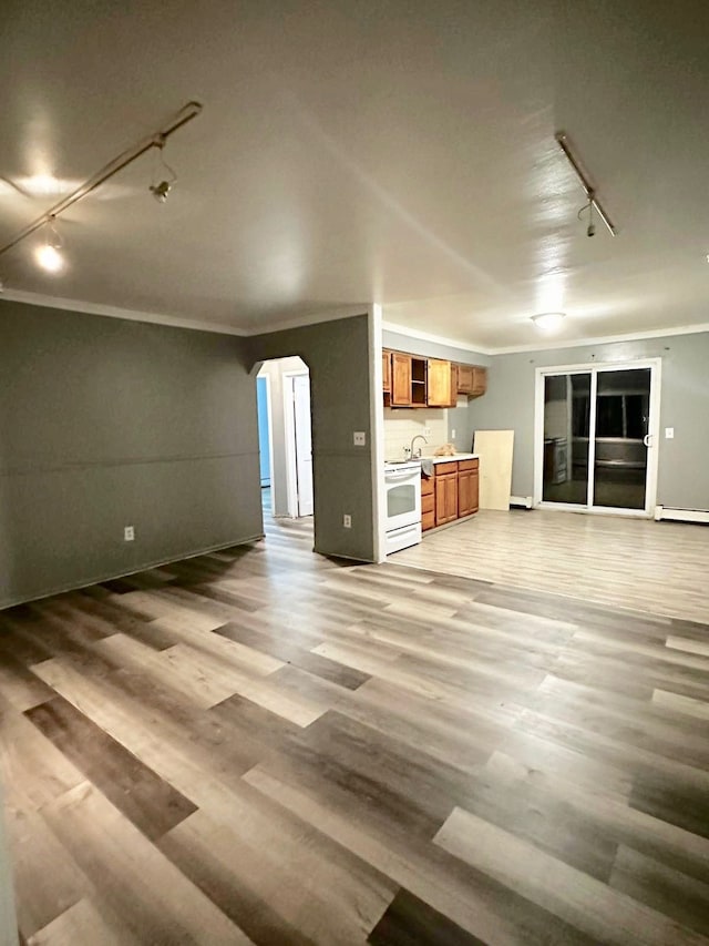 unfurnished living room featuring sink, light hardwood / wood-style flooring, a baseboard heating unit, track lighting, and ornamental molding